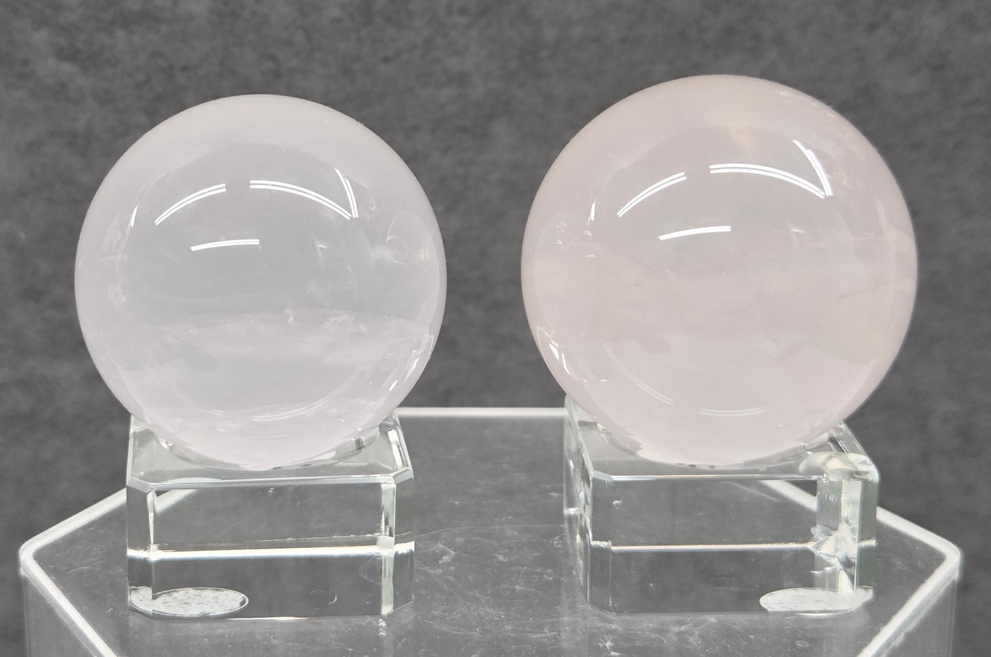 Two pale pink rose quartz spheres on stands against a gray background