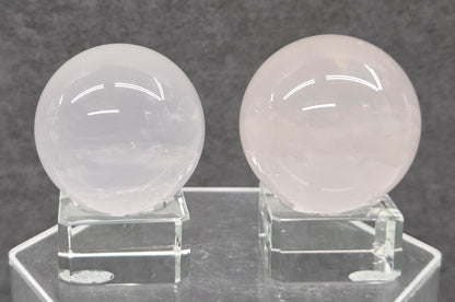 Two pale pink rose quartz spheres on stands against a gray background