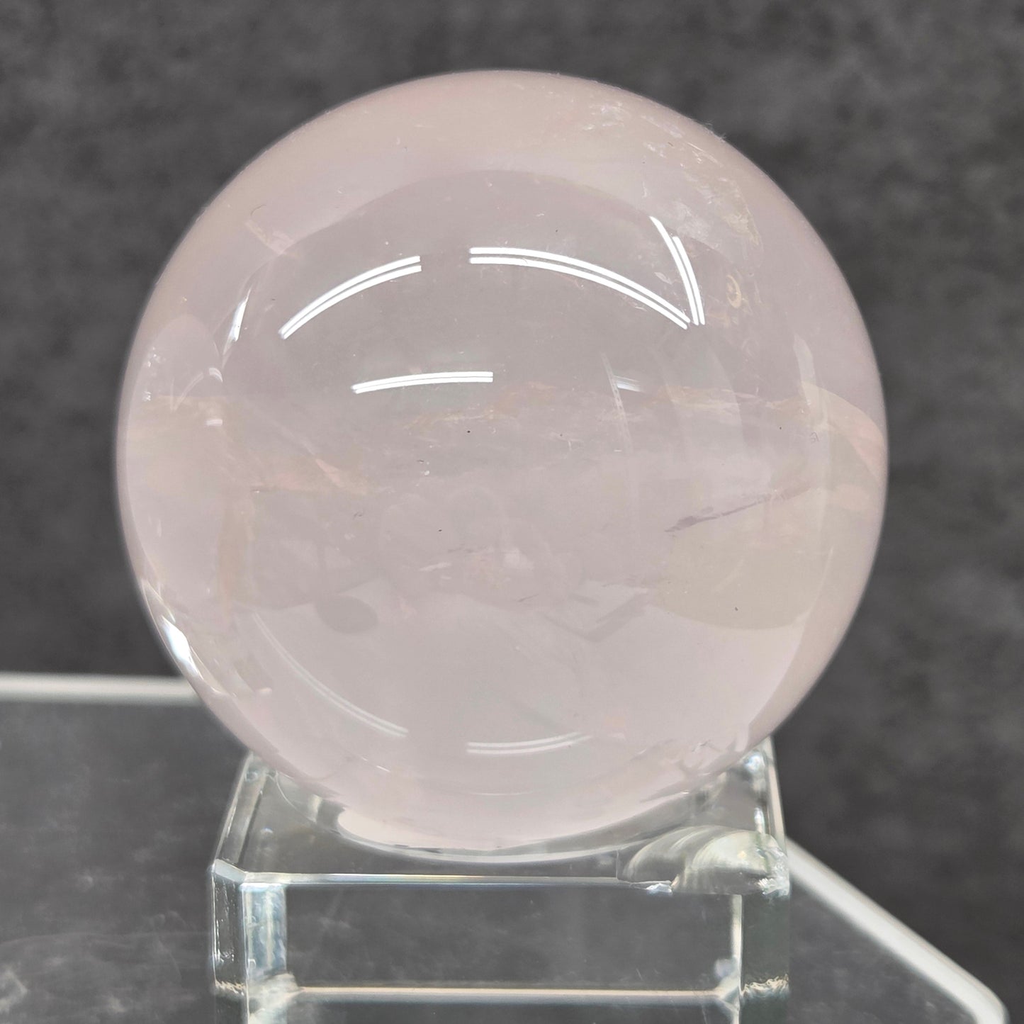 Pale pink Rose Quartz crystal sphere  on a stand against a dark background