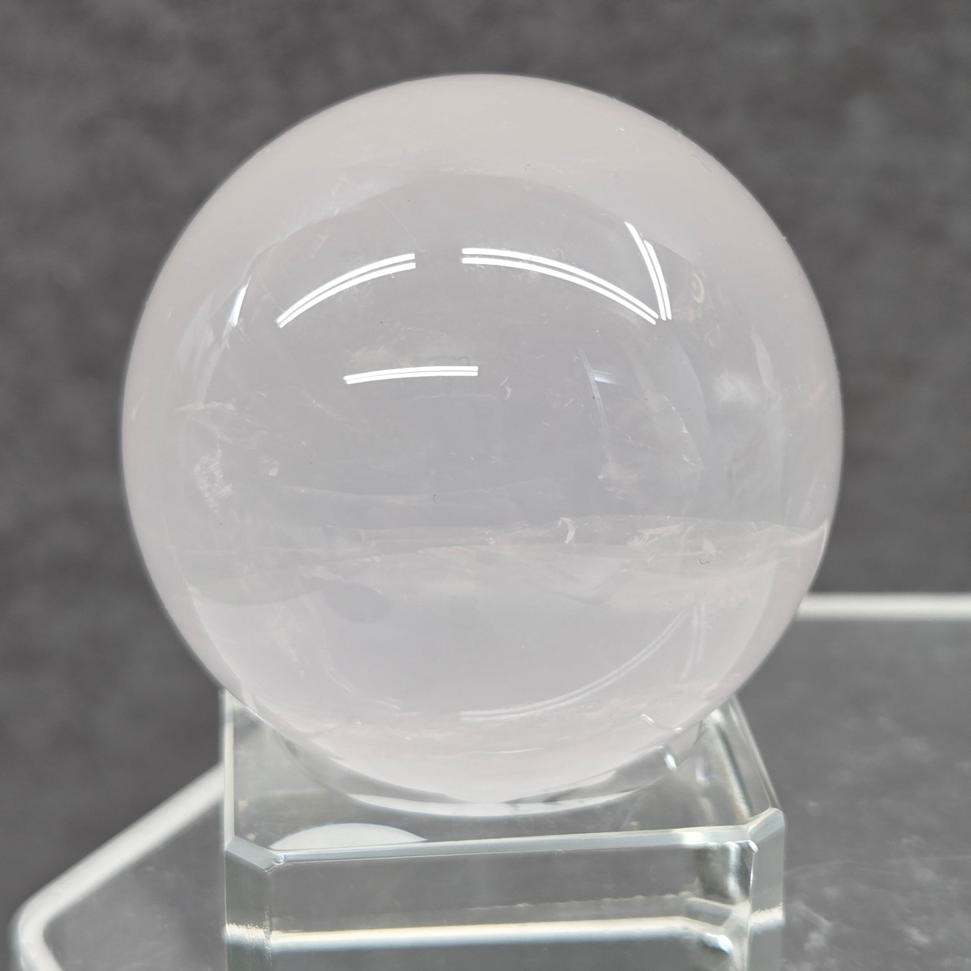 Pale pink Rose Quartz crystal sphere  on a stand against a dark background