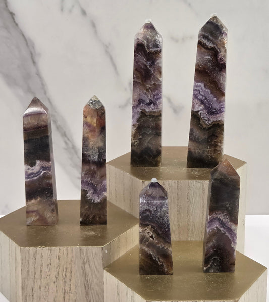 Banded crystal towers with multiple colors and inclusions on a wooden stand against a marble background