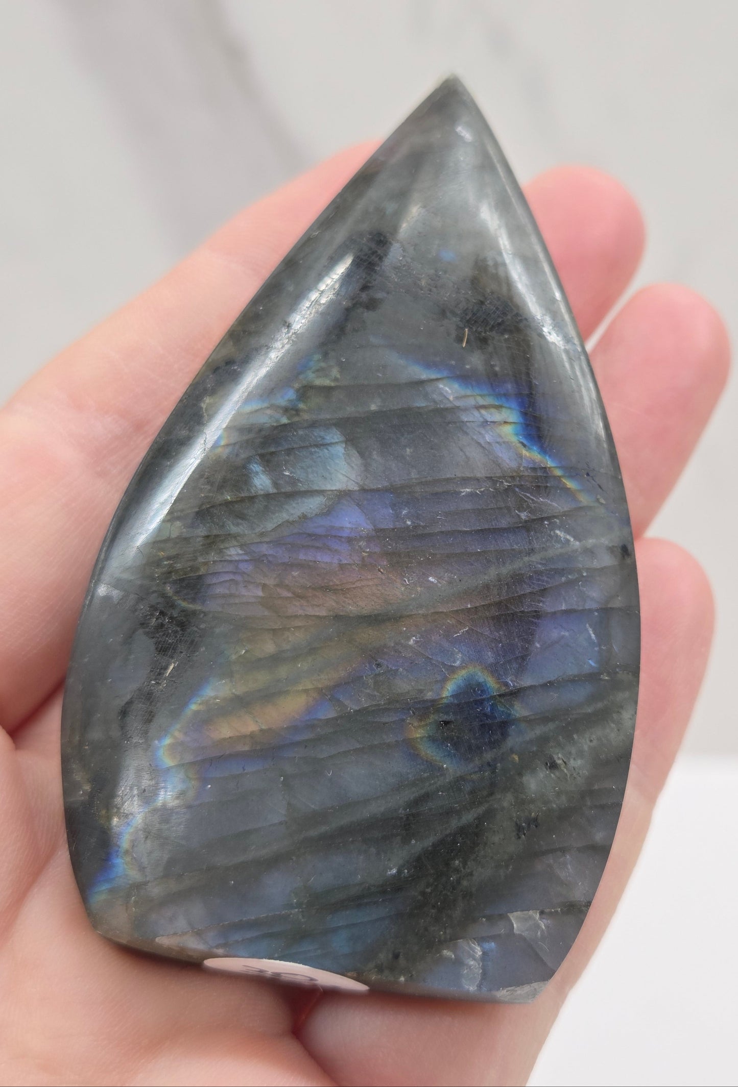 Teardrop-shaped labradorite stone held in a hand against a neutral background