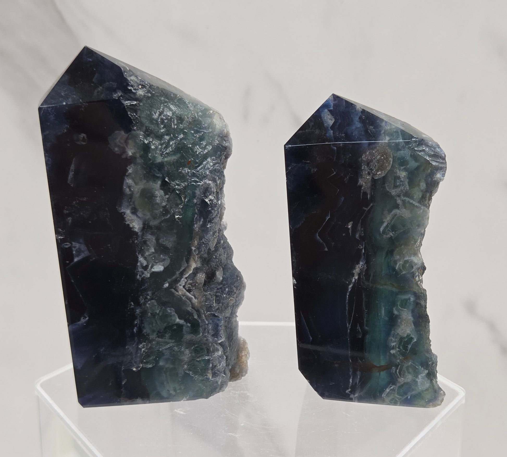 Two fluorite crystal towers on a clear stand against a marble background