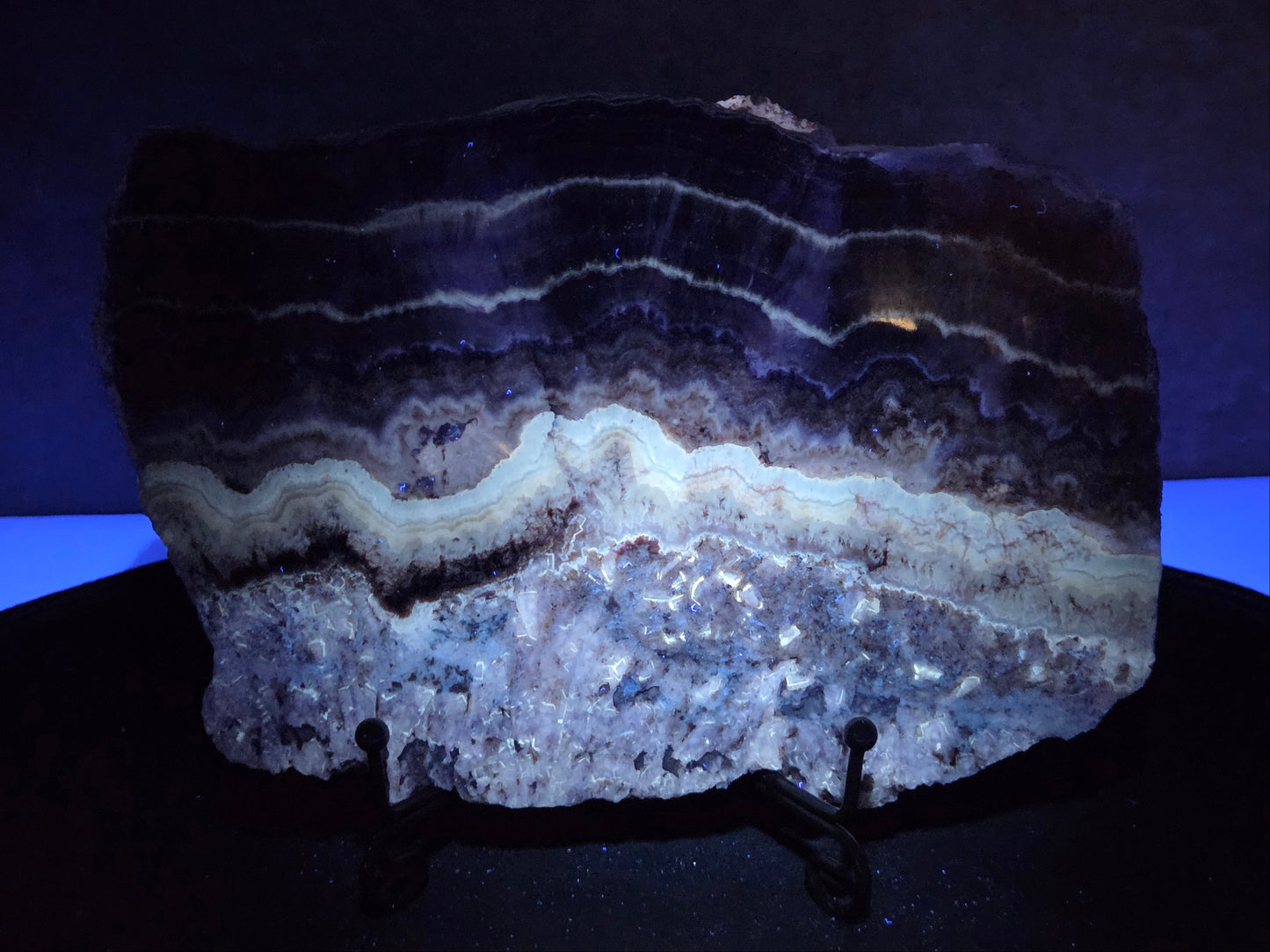 Banded crystal slice with multiple colors and inclusions on a stand under UV light