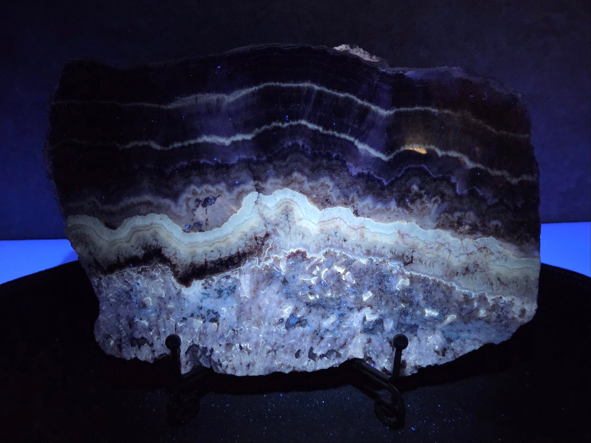 Banded crystal slice with multiple colors and inclusions on a stand under UV light