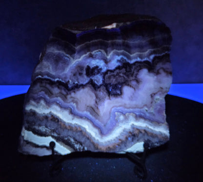 Banded crystal slice with multiple colors and inclusions on a stand under UV light
