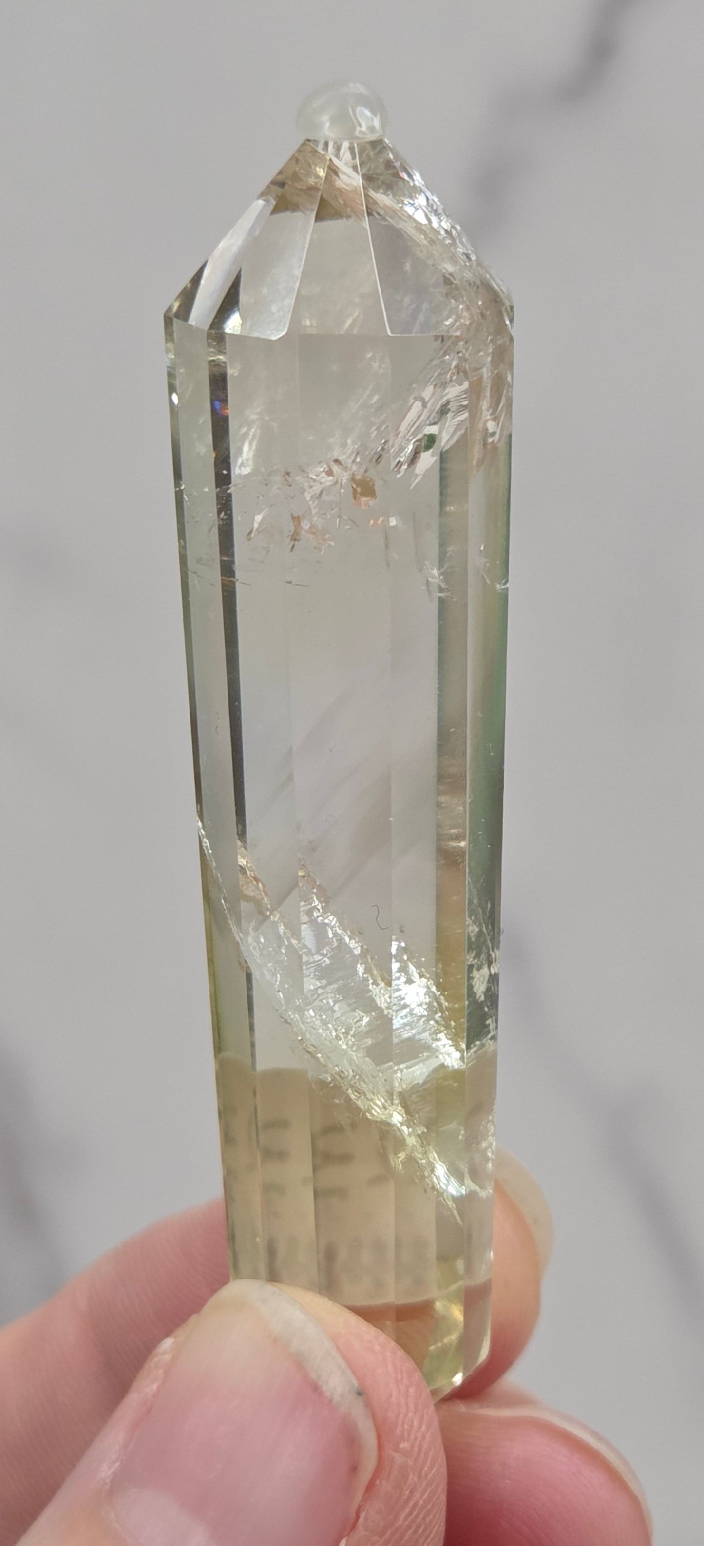 Clear crystal held by a hand against a neutral background