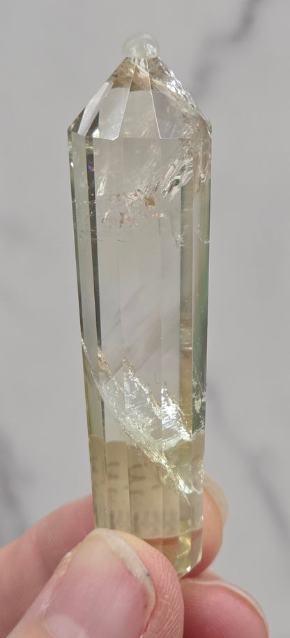 Clear crystal held by a hand against a neutral background