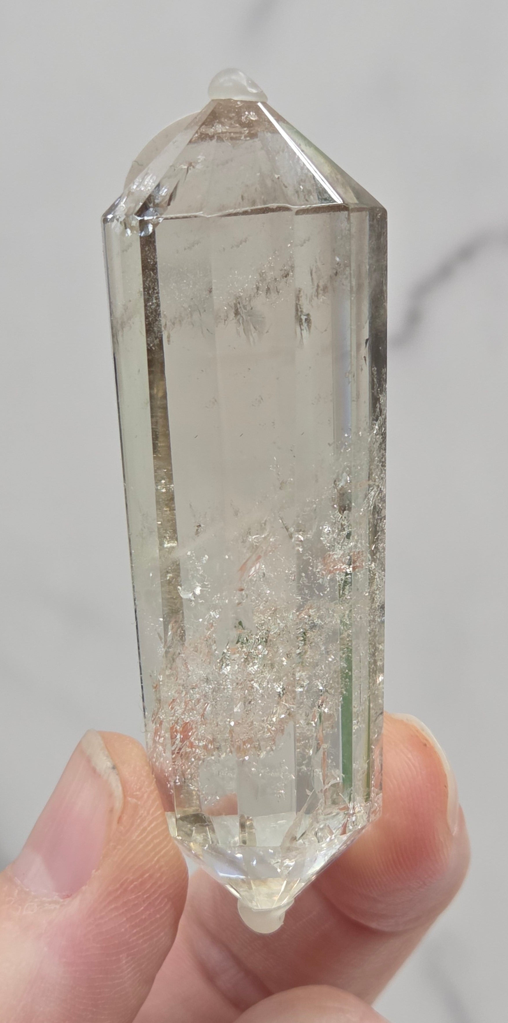 Clear crystal held by a hand against a neutral background