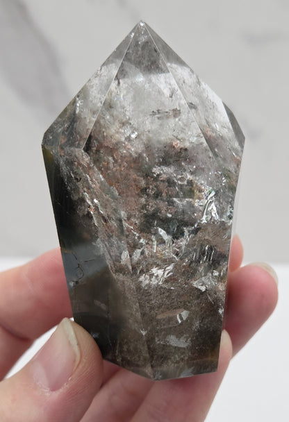Hand holding a Garden Quartz crystal with a white background