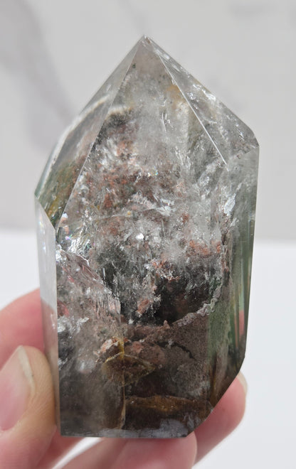 Hand holding a Garden Quartz crystal with visible minerals against a white background