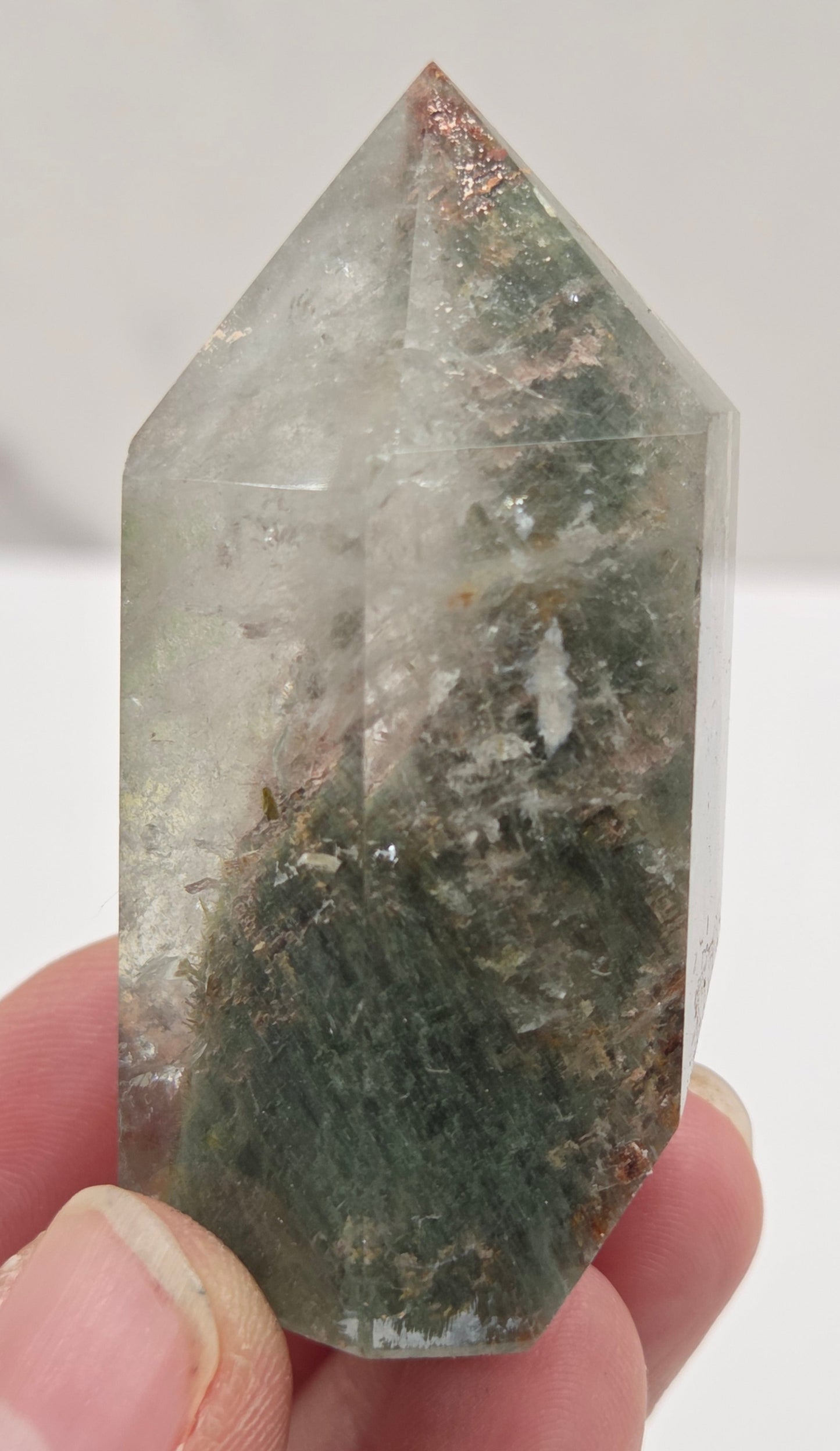 Person holding a Garden Quartz  crystal with a clear and greenish tint against a white background