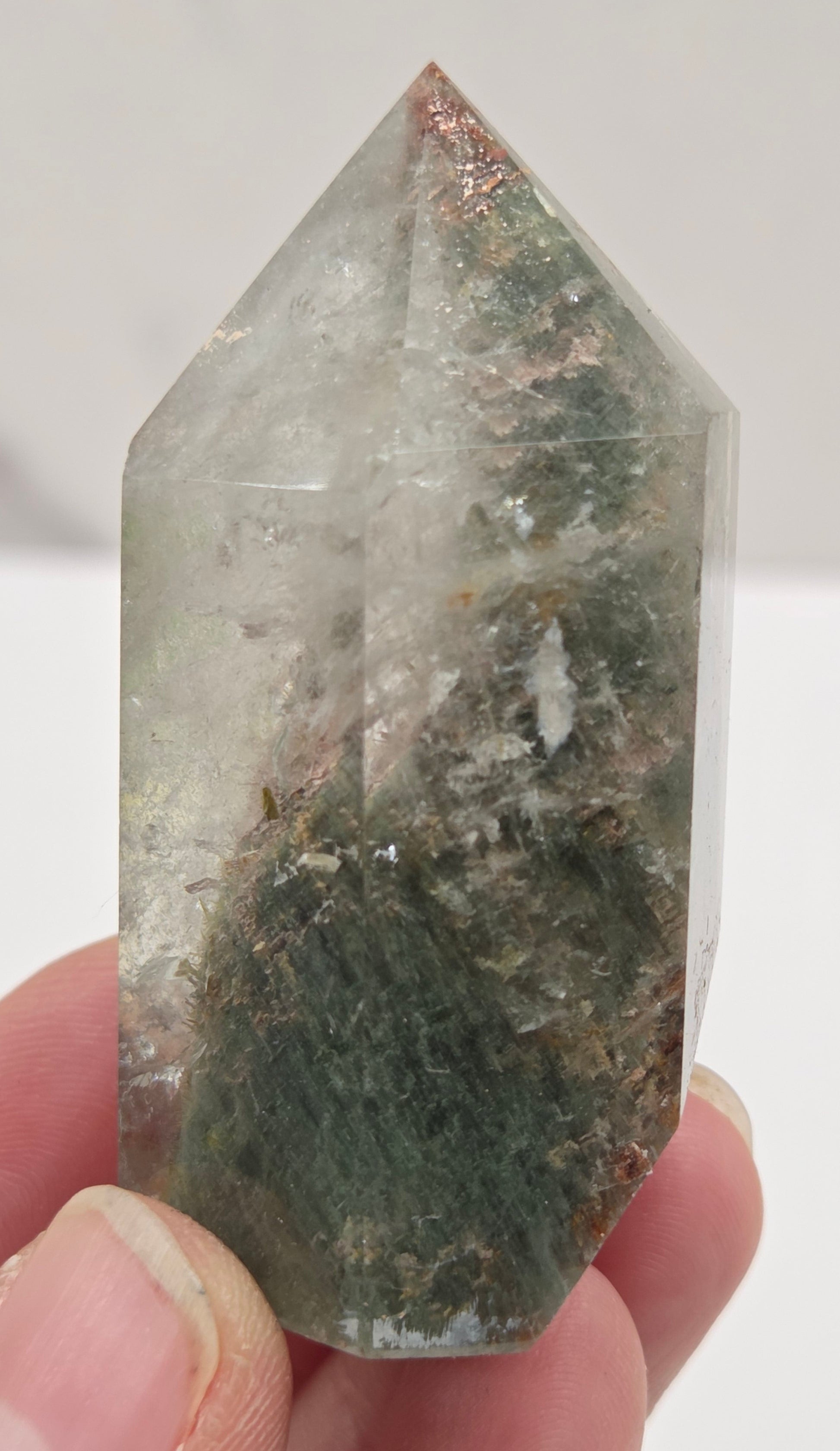 Person holding a Garden Quartz  crystal with a clear and greenish tint against a white background