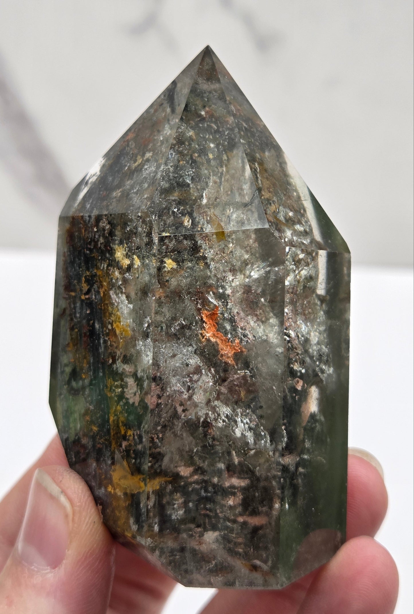 Hand holding a Garden Quartz crystal with visible minerals and colors