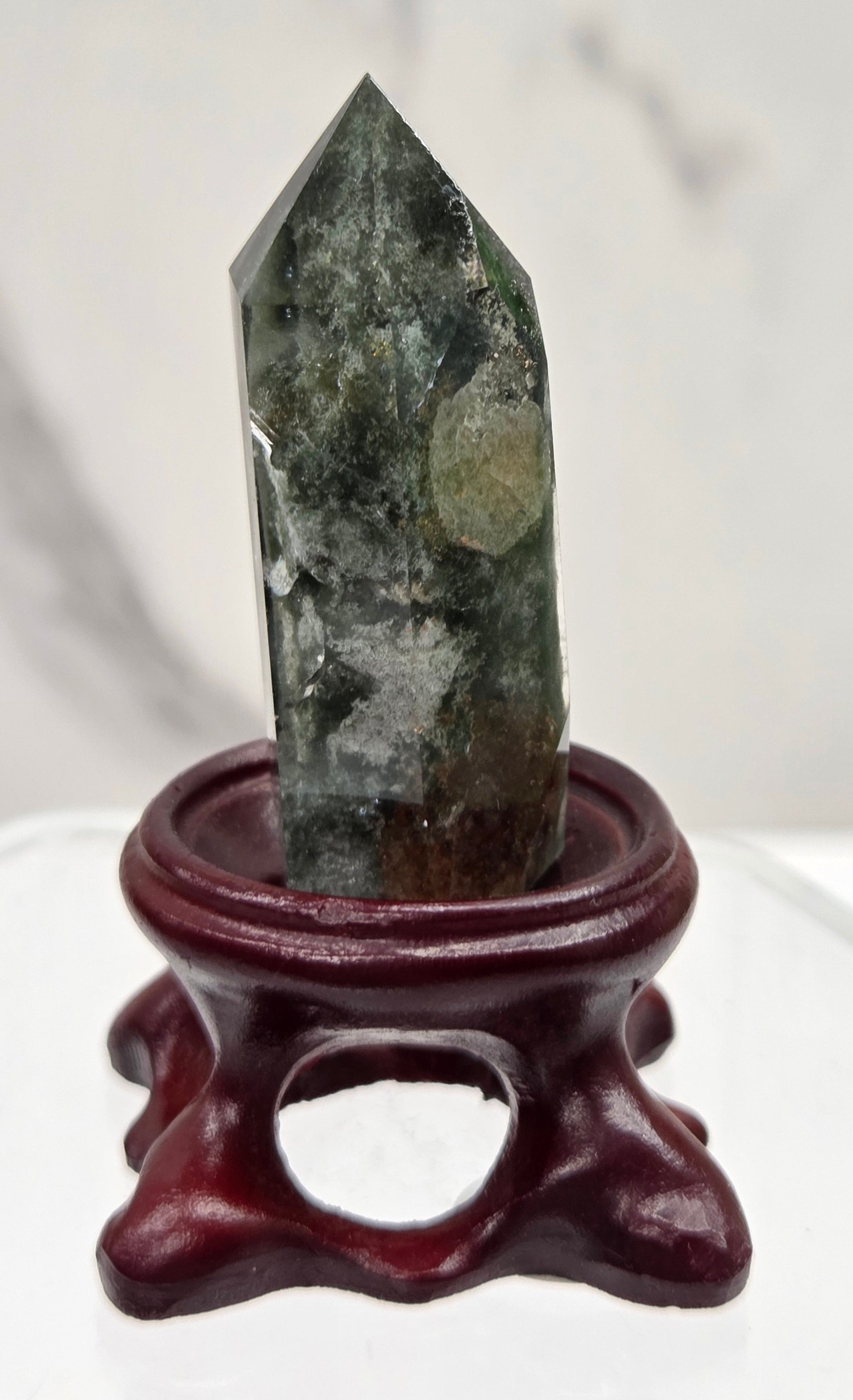 A clear Garden Quartz crystal with inclusions, mounted on a wooden stand with a circular cut-out at the base.