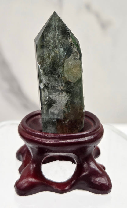 A clear Garden Quartz crystal with inclusions, mounted on a wooden stand with a circular cut-out at the base.