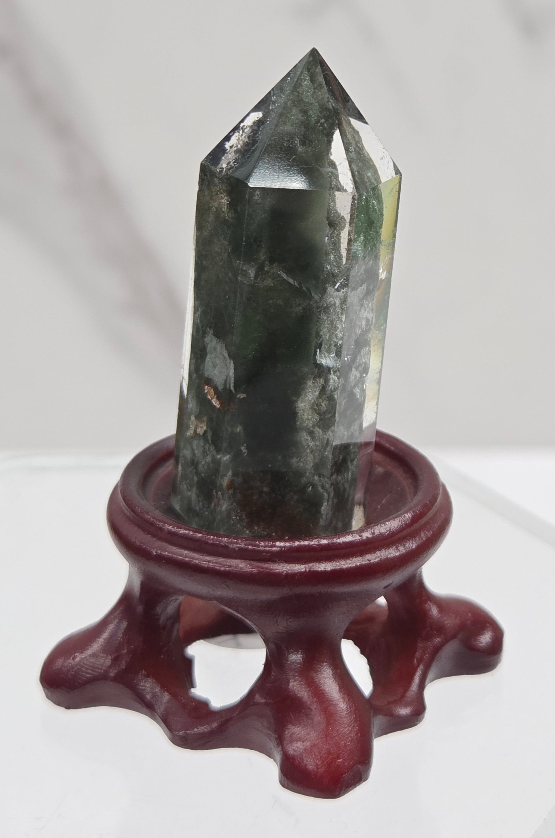 A clear Garden Quartz crystal with inclusions, mounted on a wooden stand with a circular cut-out at the base.