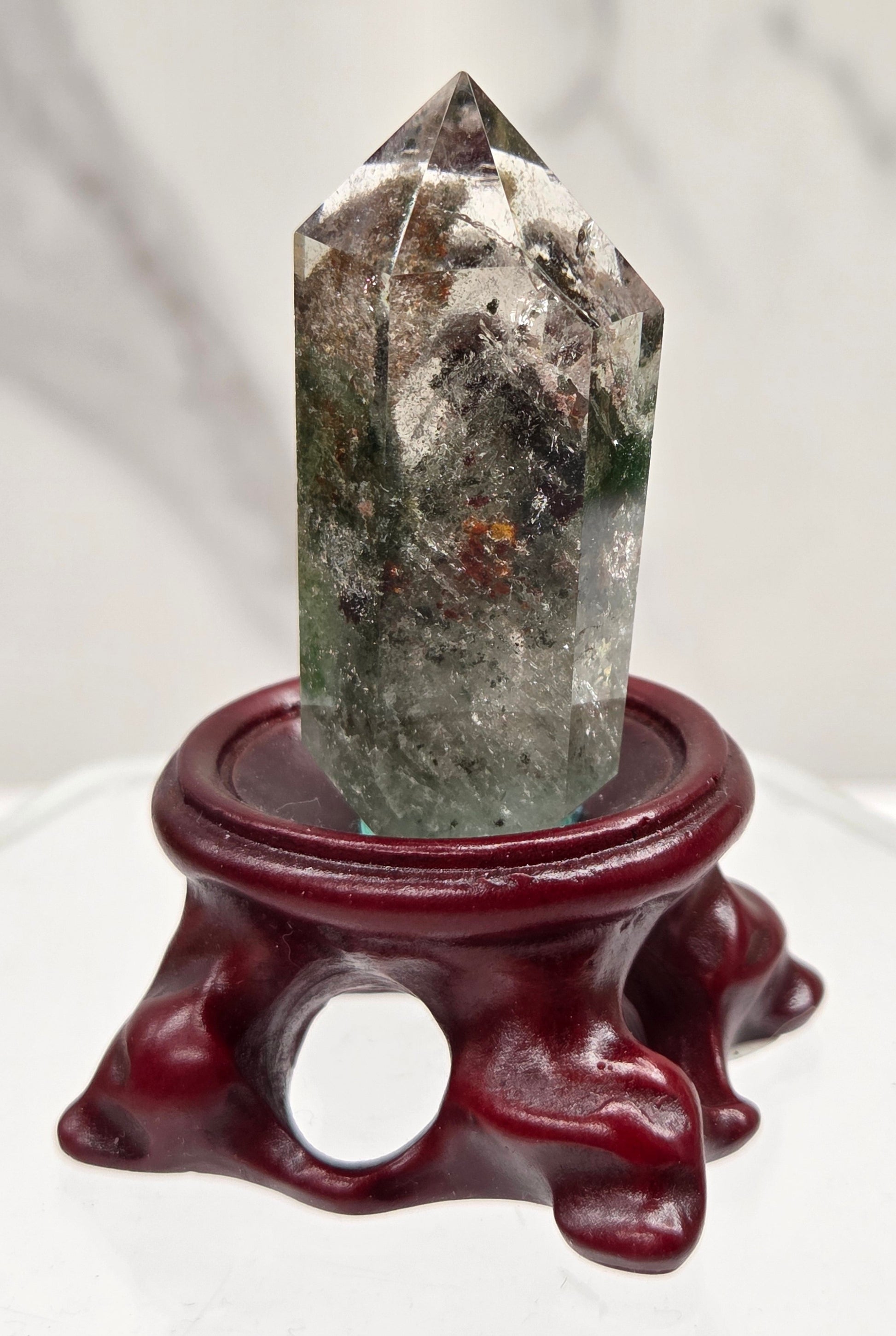 A clear Garden Quartz crystal with inclusions, mounted on a wooden stand with a circular cut-out at the base.