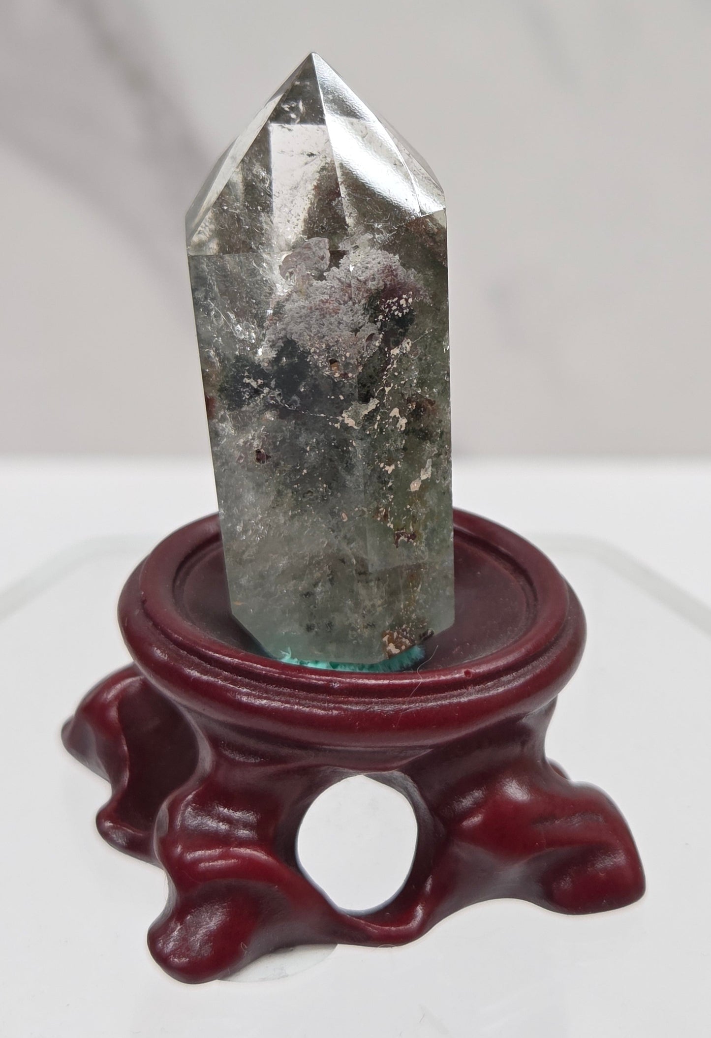 A clear Garden Quartz crystal with inclusions, mounted on a wooden stand with a circular cut-out at the base.