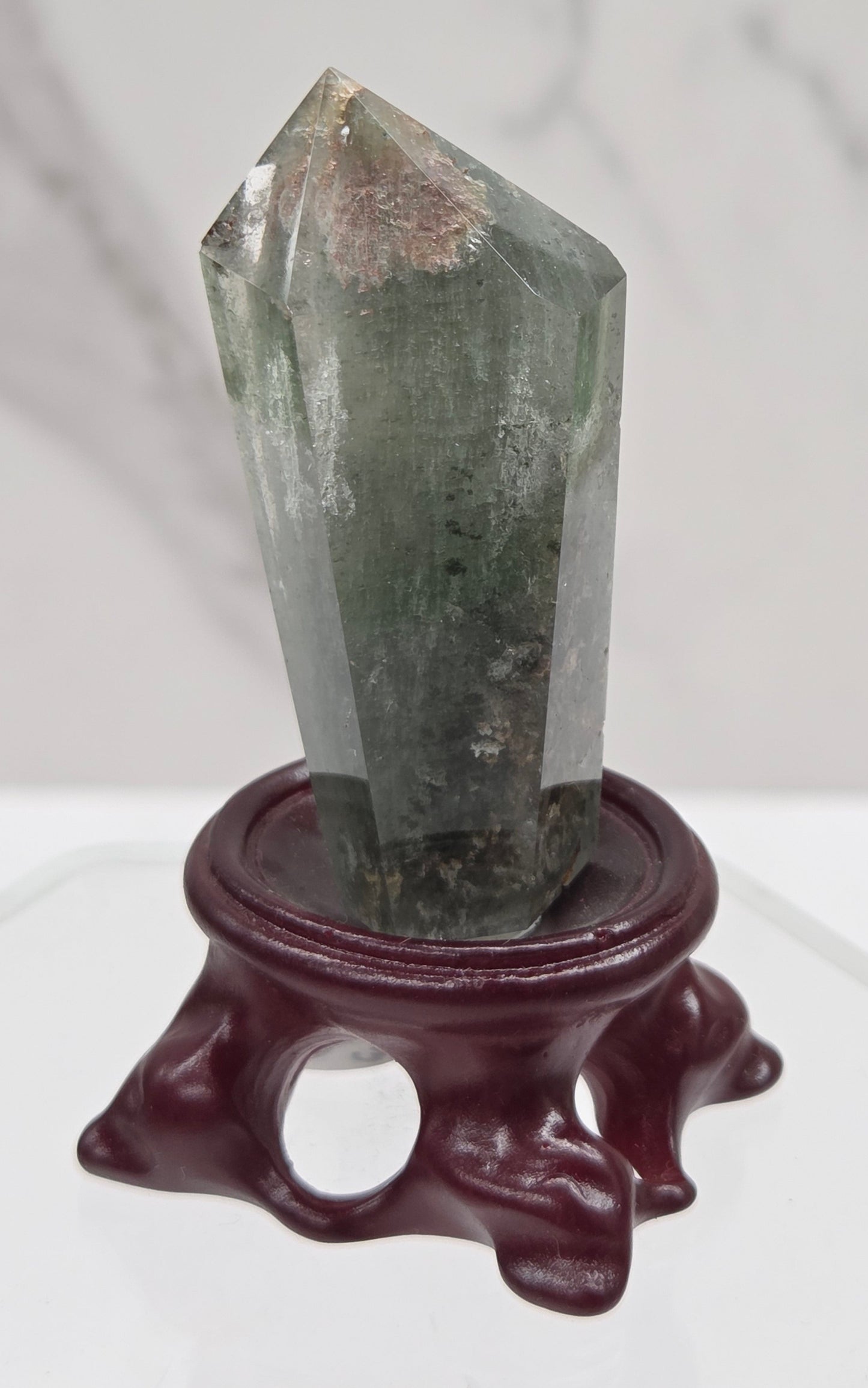 A clear Garden Quartz crystal with inclusions, mounted on a wooden stand with a circular cut-out at the base.
