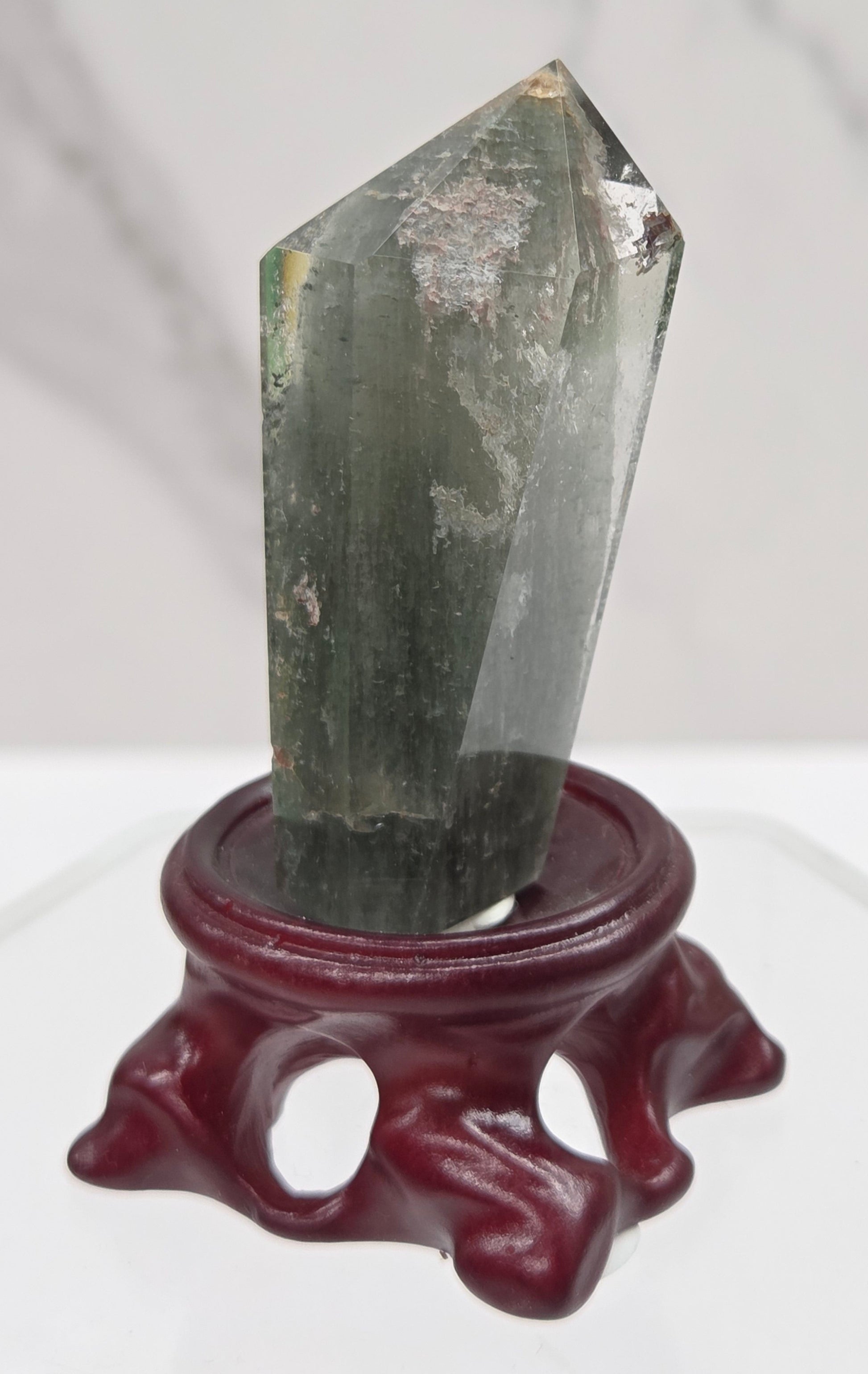 A clear Garden Quartz crystal with inclusions, mounted on a wooden stand with a circular cut-out at the base.