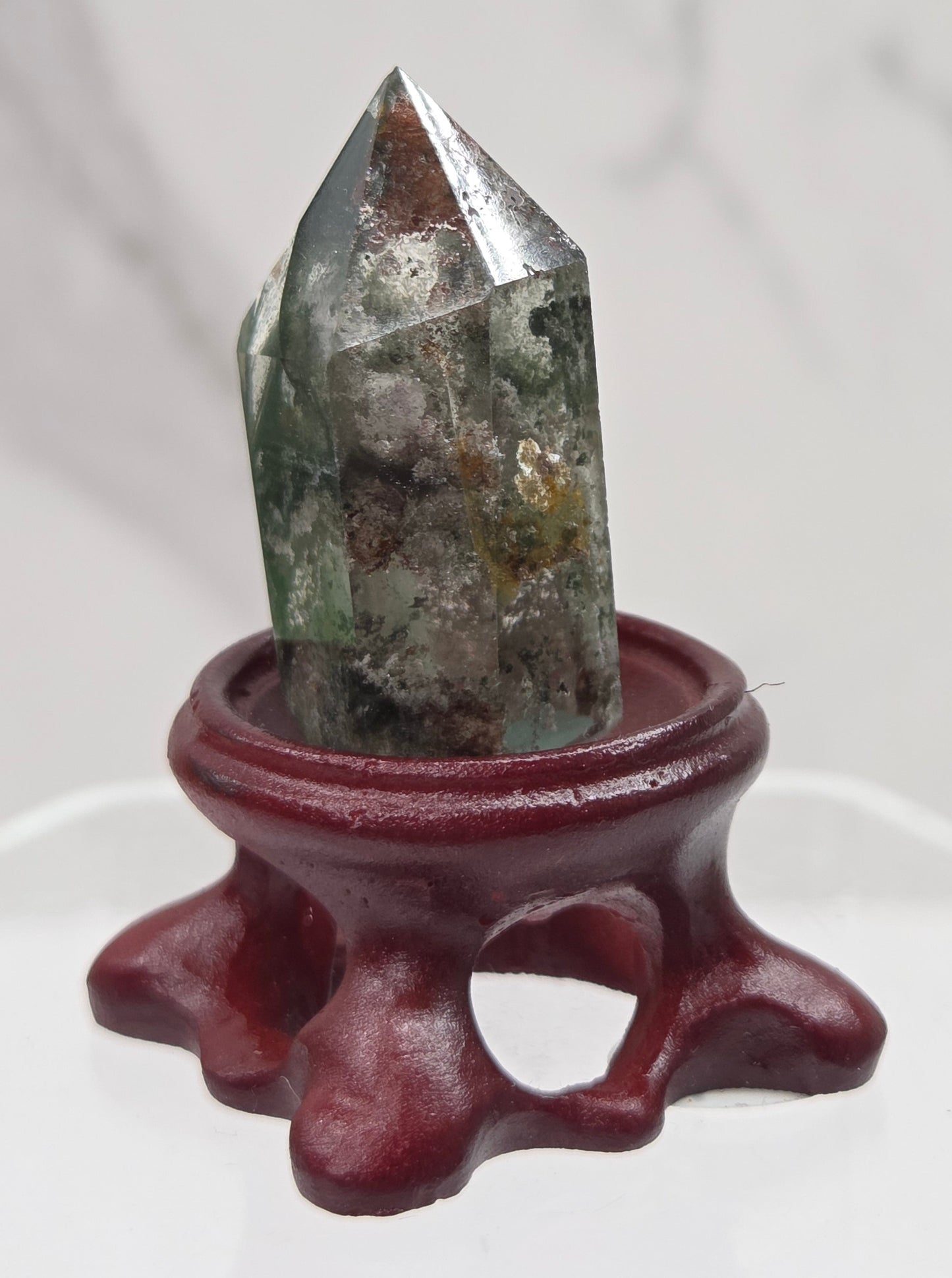 A clear Garden Quartz crystal with inclusions, mounted on a wooden stand with a circular cut-out at the base.