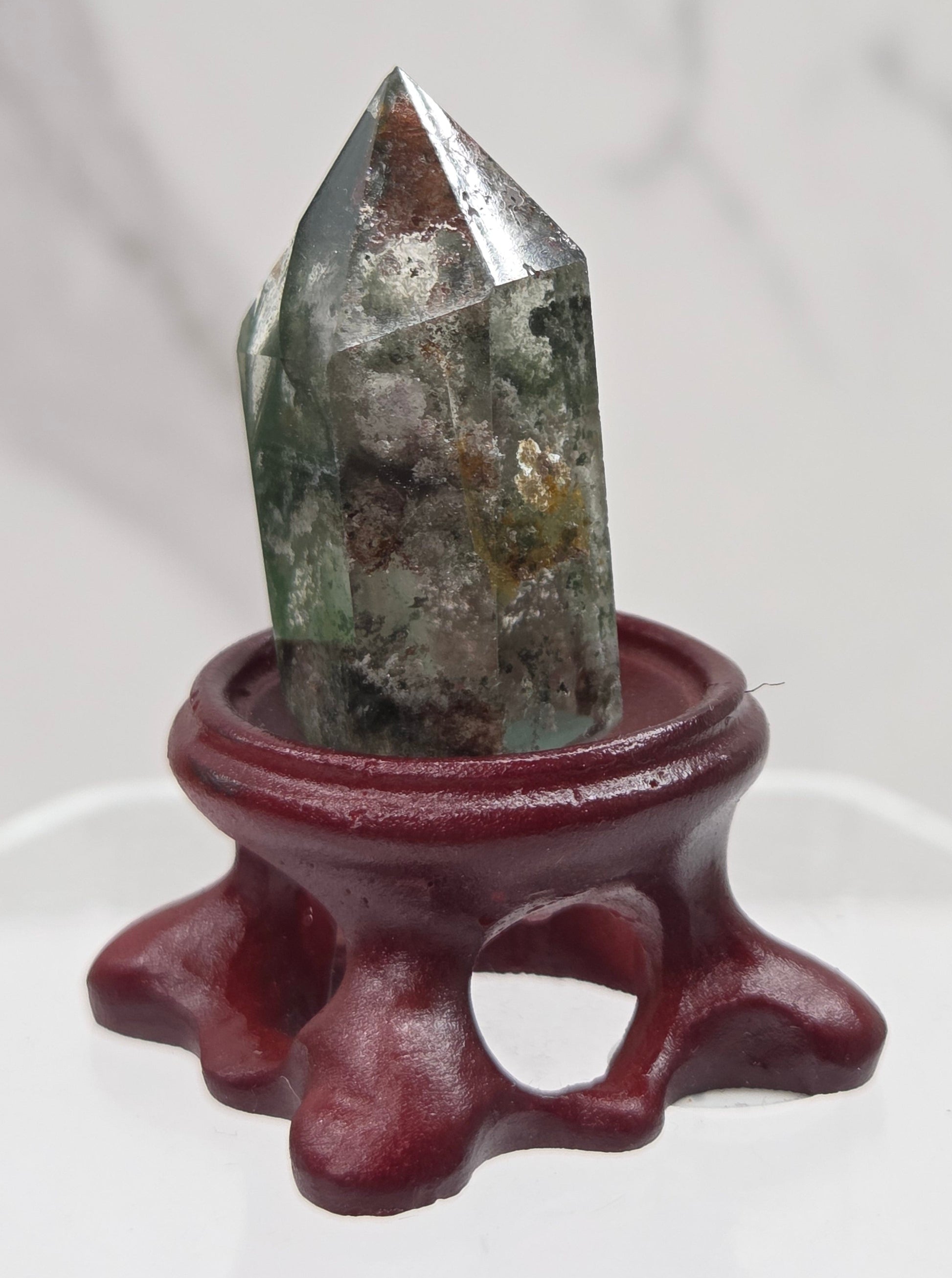 A clear Garden Quartz crystal with inclusions, mounted on a wooden stand with a circular cut-out at the base.