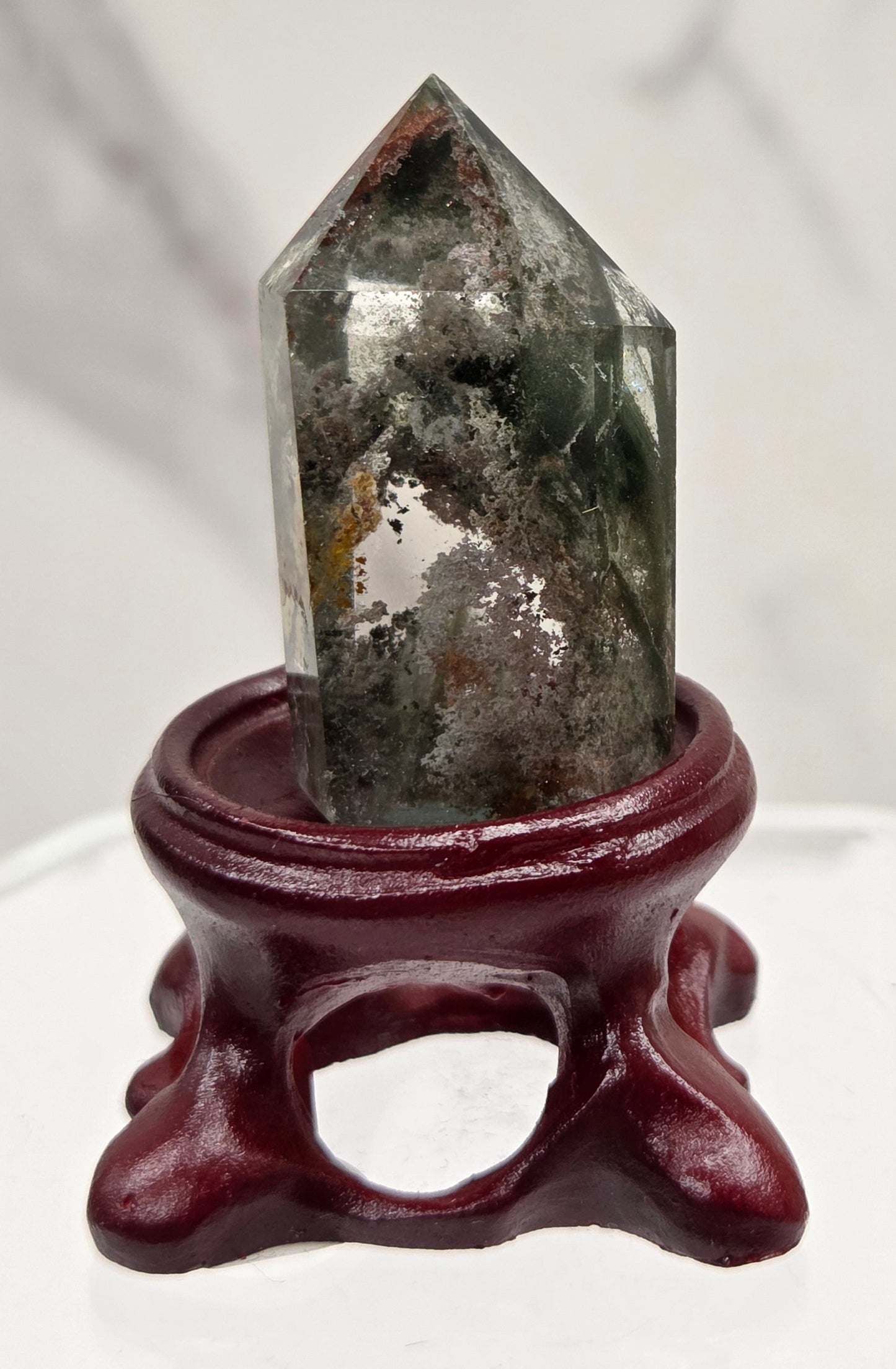 A clear Garden Quartz crystal with inclusions, mounted on a wooden stand with a circular cut-out at the base.
