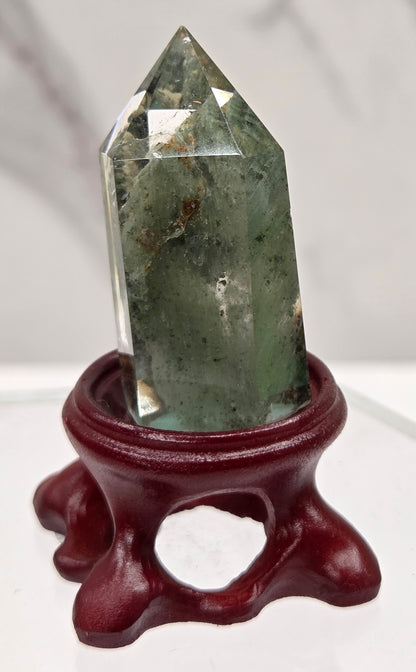 A clear Garden Quartz crystal with inclusions, mounted on a wooden stand with a circular cut-out at the base.