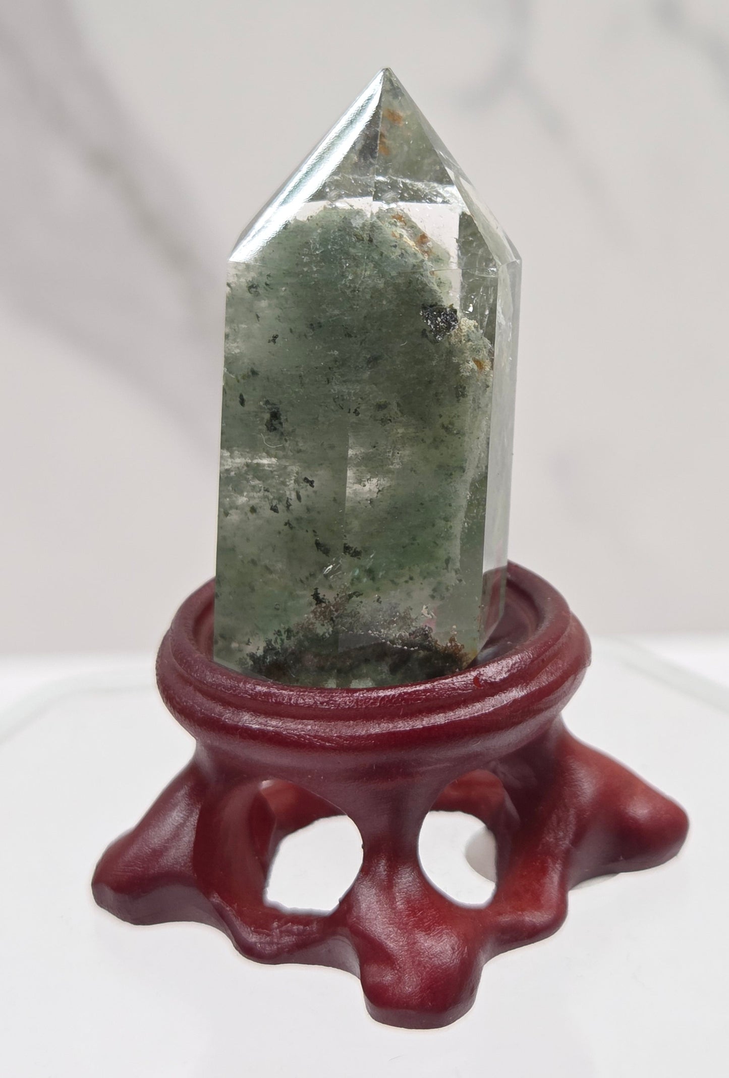 A clear Garden Quartz crystal with inclusions, mounted on a wooden stand with a circular cut-out at the base.