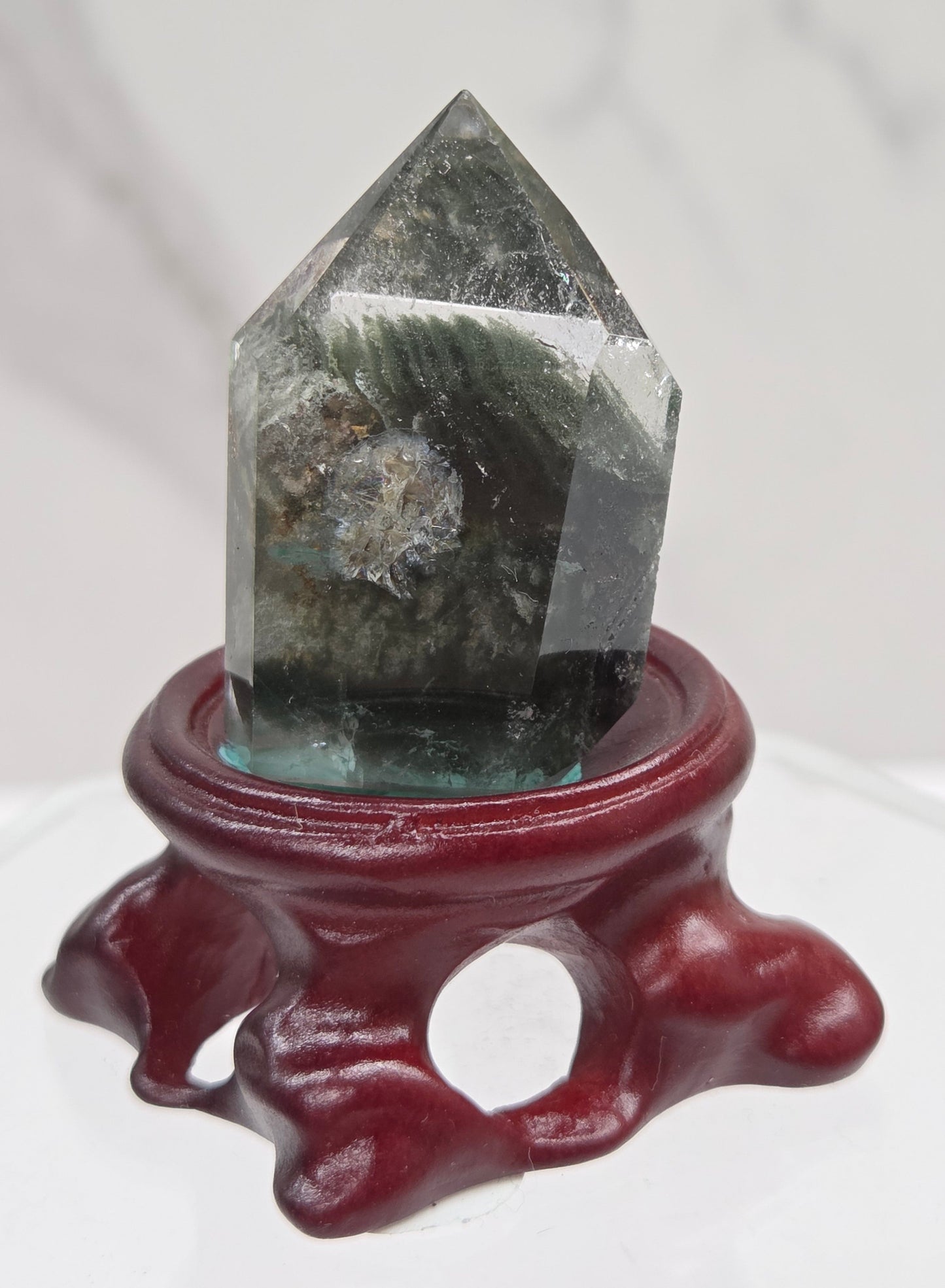 A clear Garden Quartz crystal with inclusions, mounted on a wooden stand with a circular cut-out at the base.