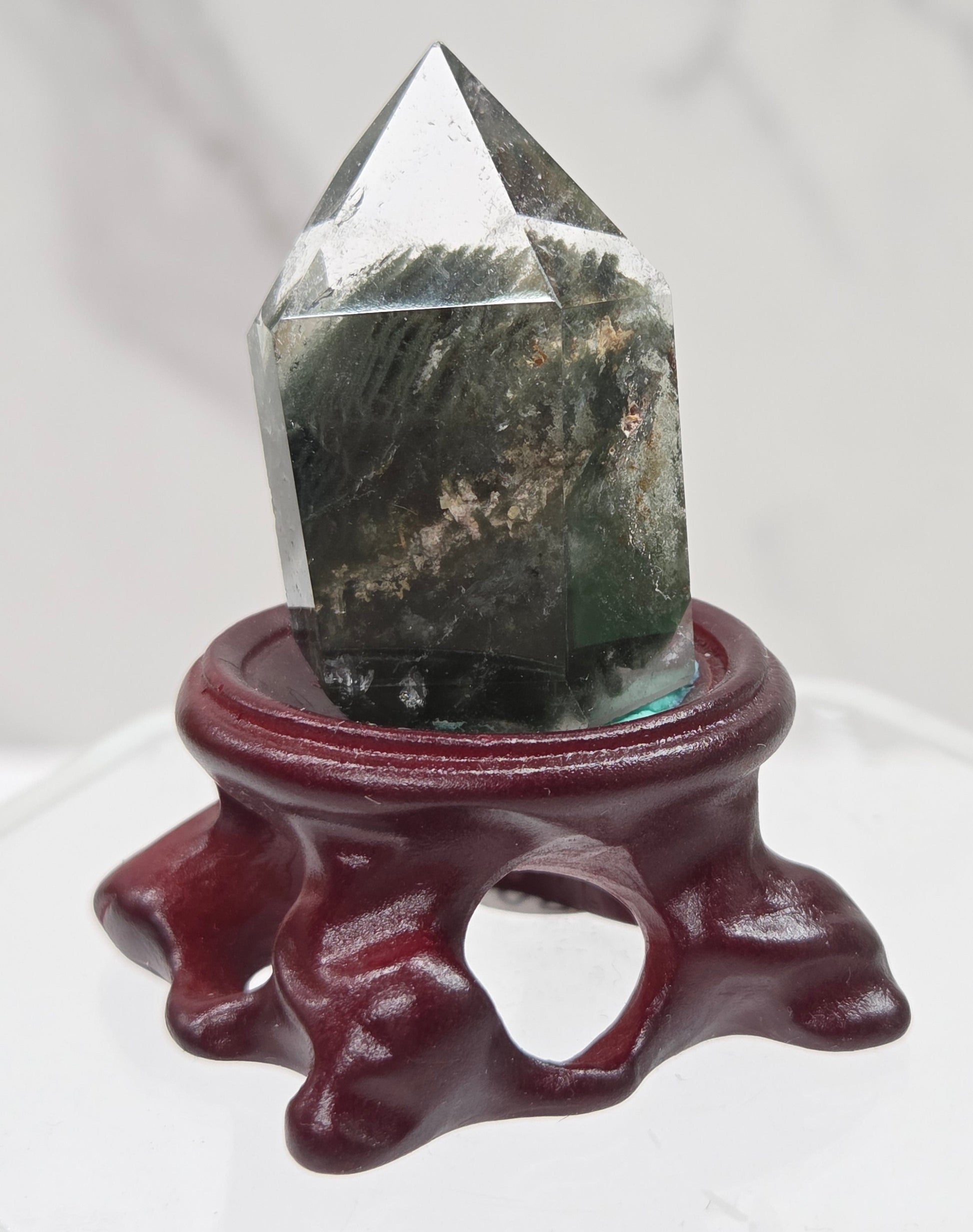A clear Garden Quartz crystal with inclusions, mounted on a wooden stand with a circular cut-out at the base.