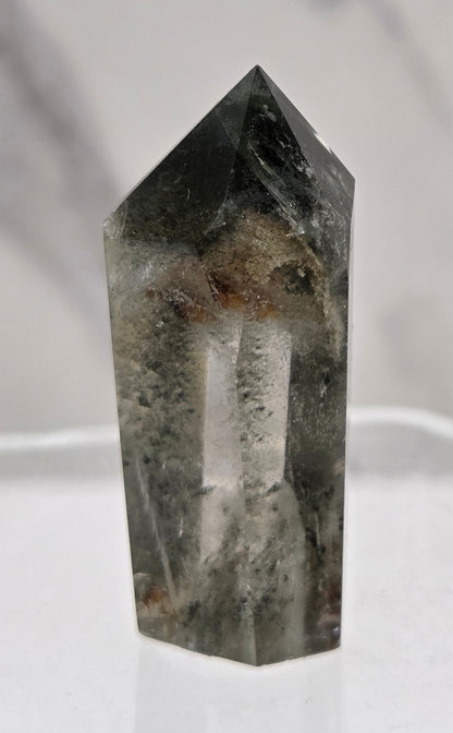Polished quartz crystal tower with inclusions displayed on a white background