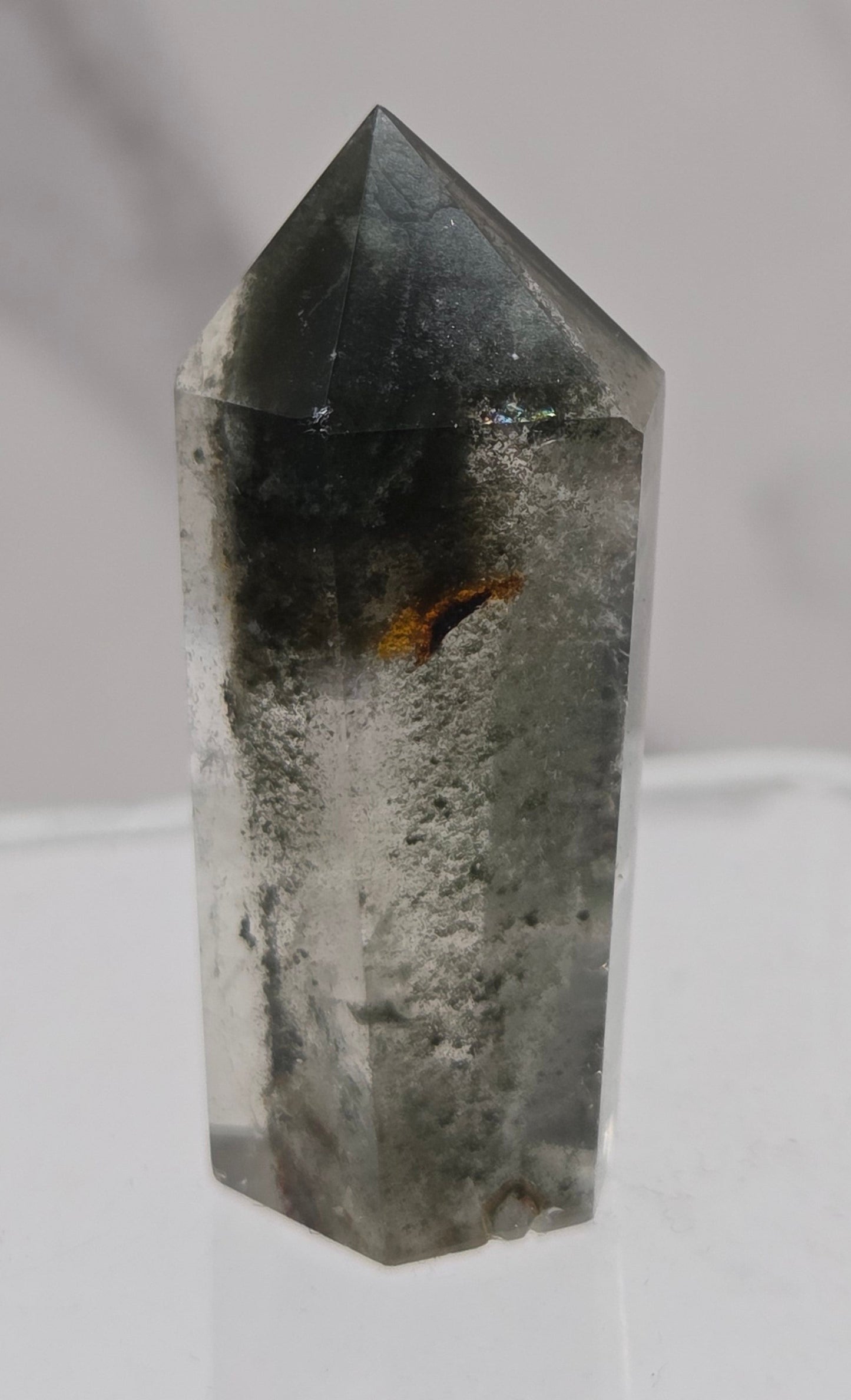 Polished quartz crystal tower with inclusions displayed on a white background
