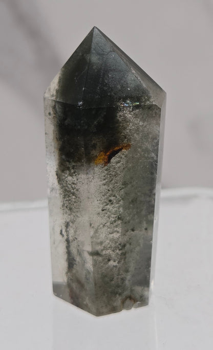Polished quartz crystal tower with inclusions displayed on a white background
