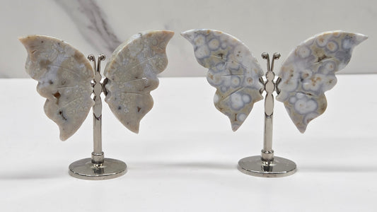 Butterfly-shaped jasper wings on stands with a marble-like texture against a neutral background