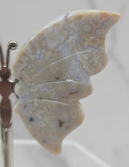 Butterfly-shaped jasper wings on stands with a marble-like texture against a neutral background