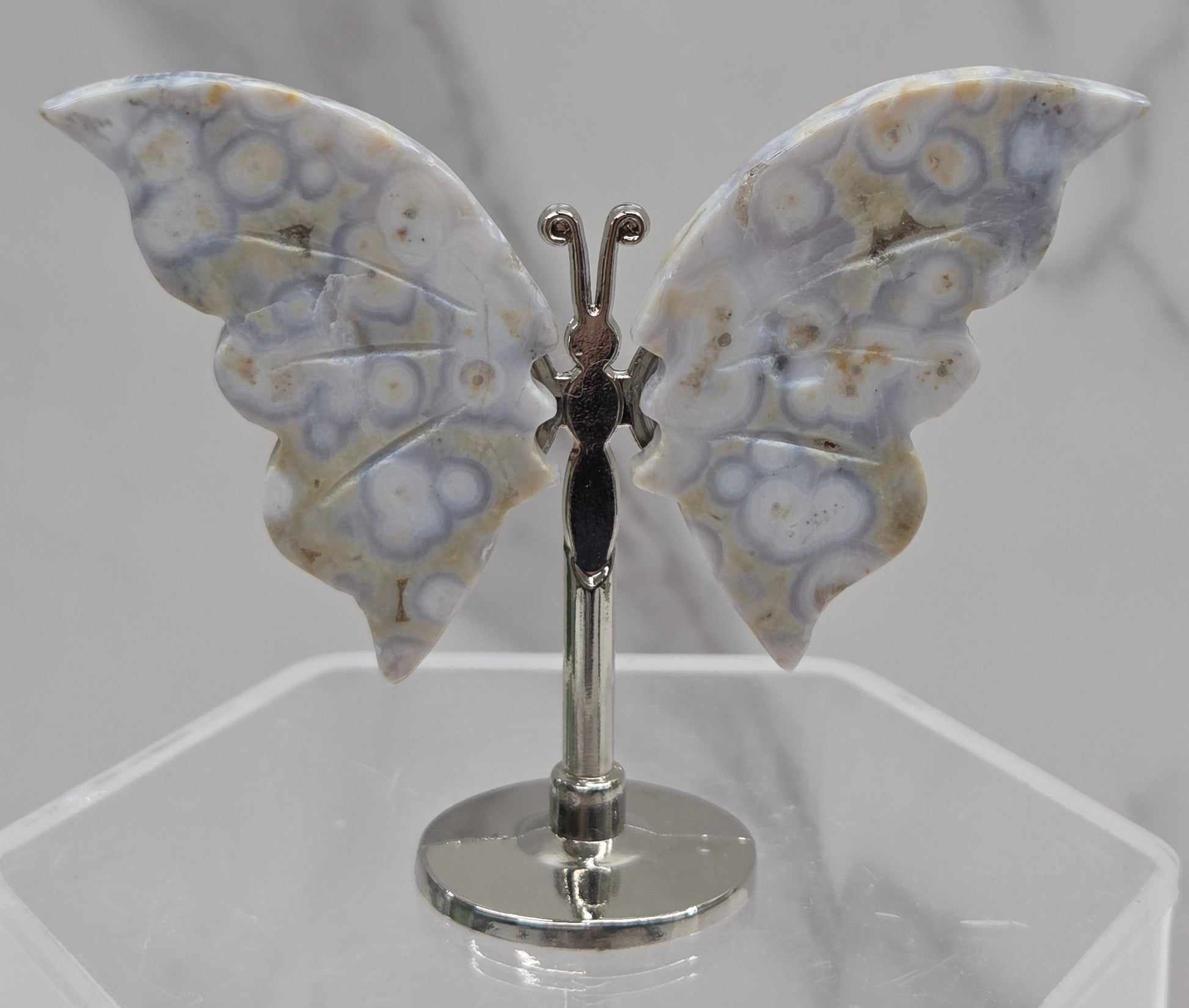 Butterfly-shaped jasper wings on stands with a marble-like texture against a neutral background