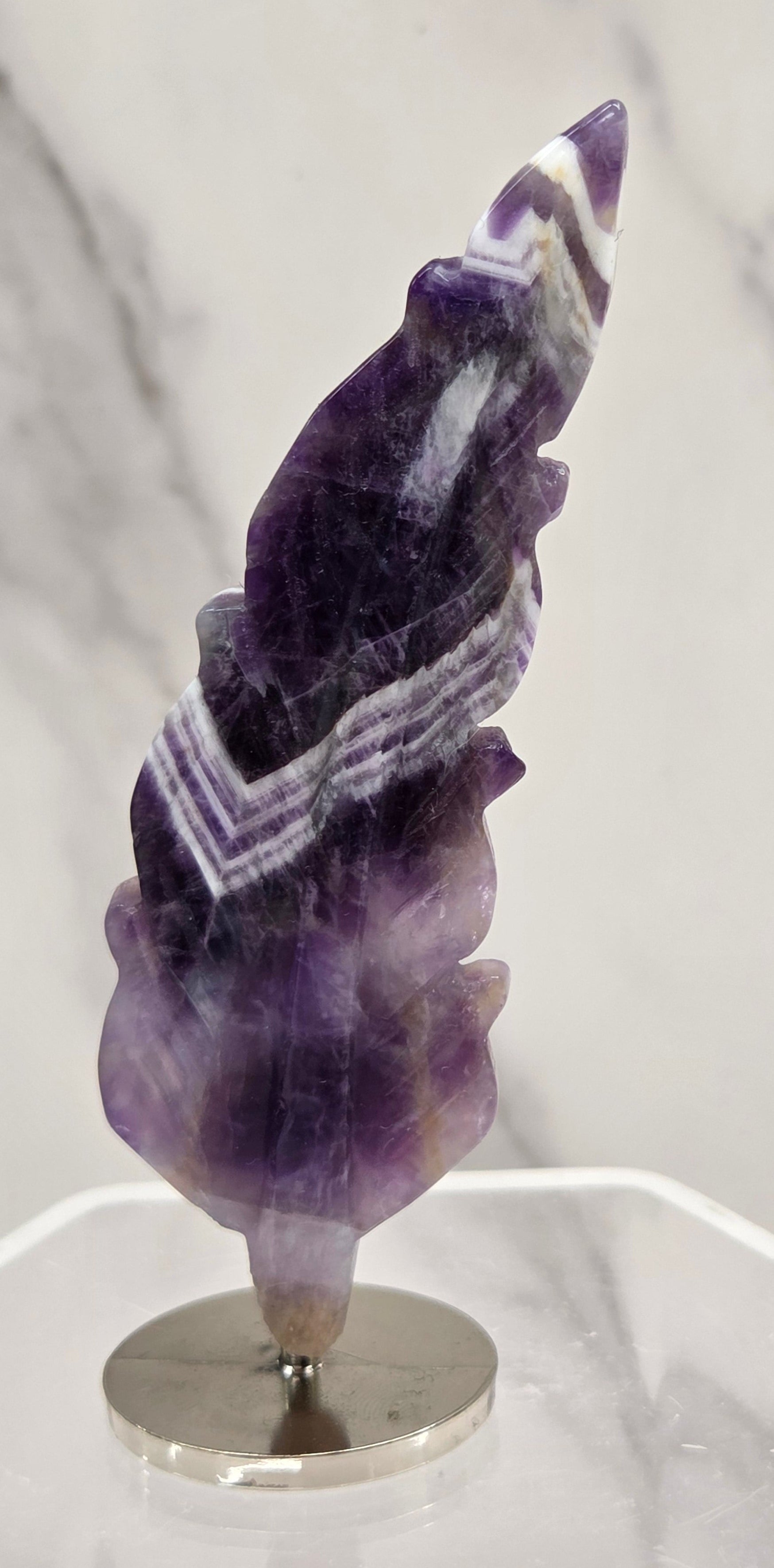Amethyst feather shaped crystal on a white stand against a marble background