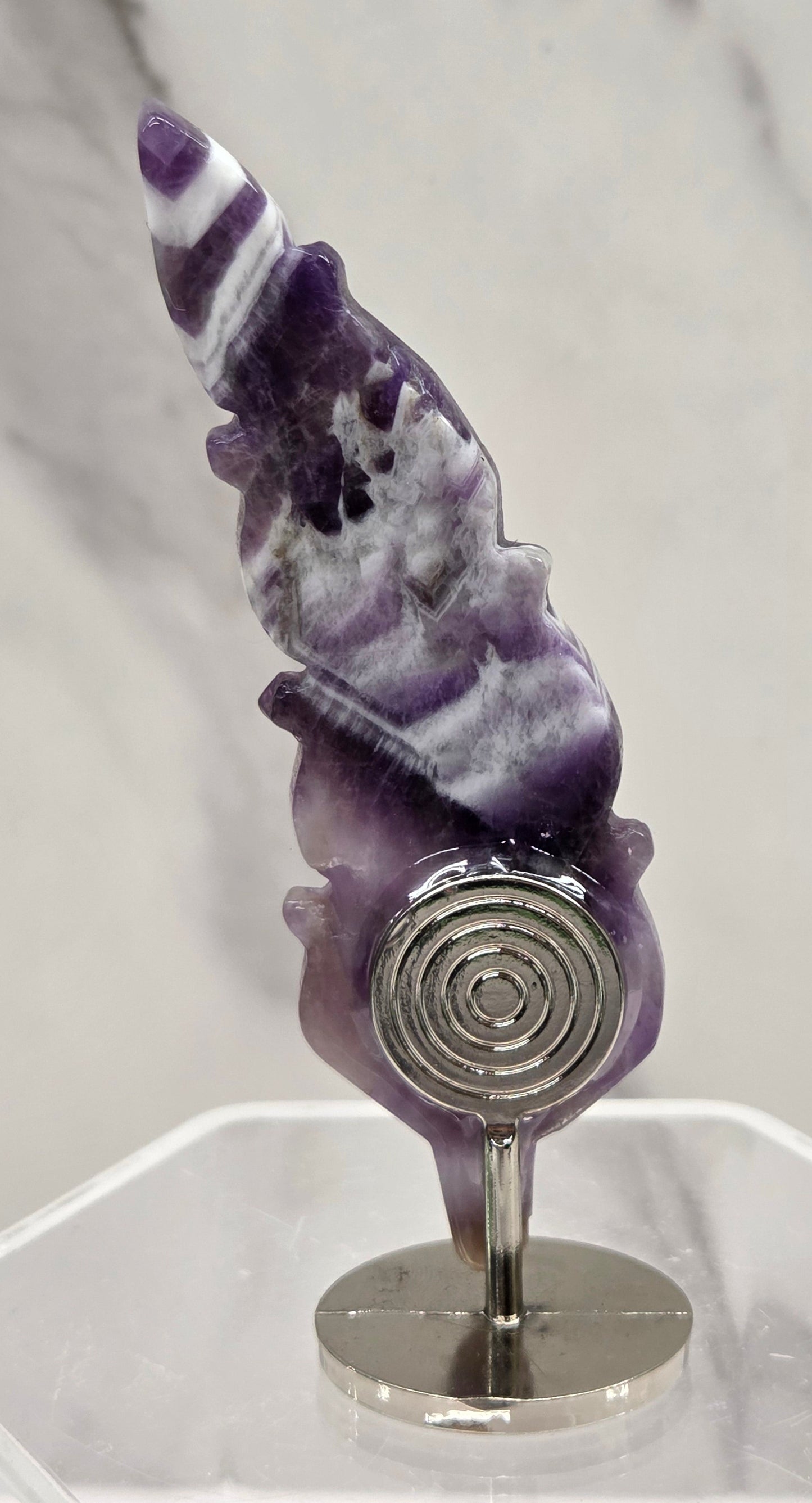 Amethyst feather shaped crystal on a white stand against a marble background