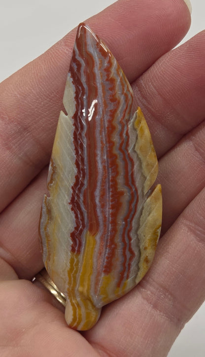 Hand holding a striped jasper feather carving with a plain background