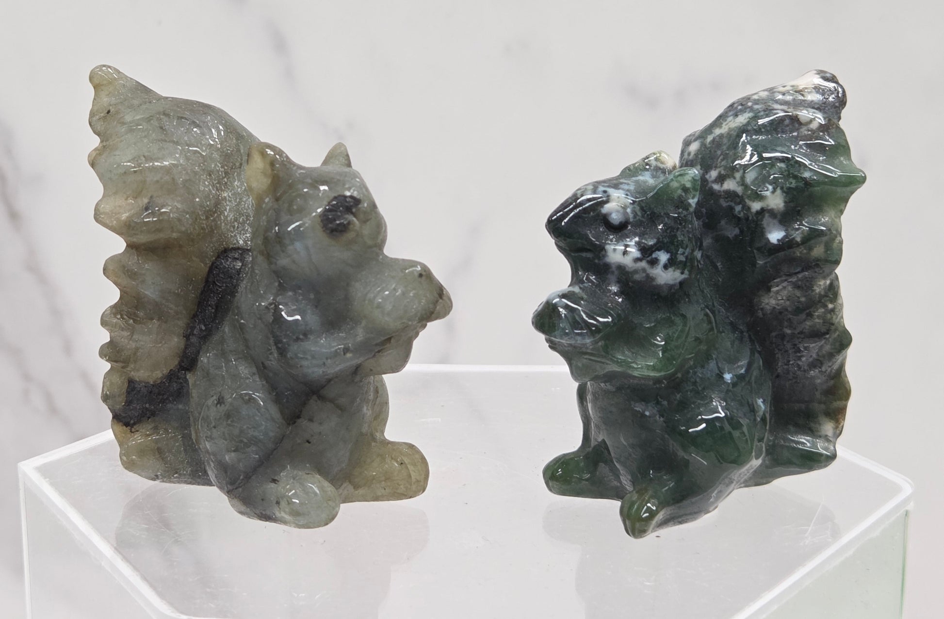 Two crystal squirrel carvings on a clear stand with a white background