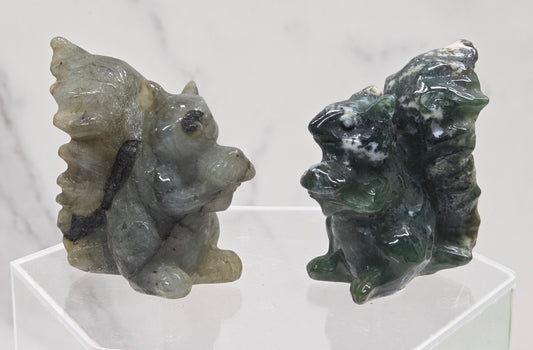 Two crystal squirrel carvings on a clear stand with a white background