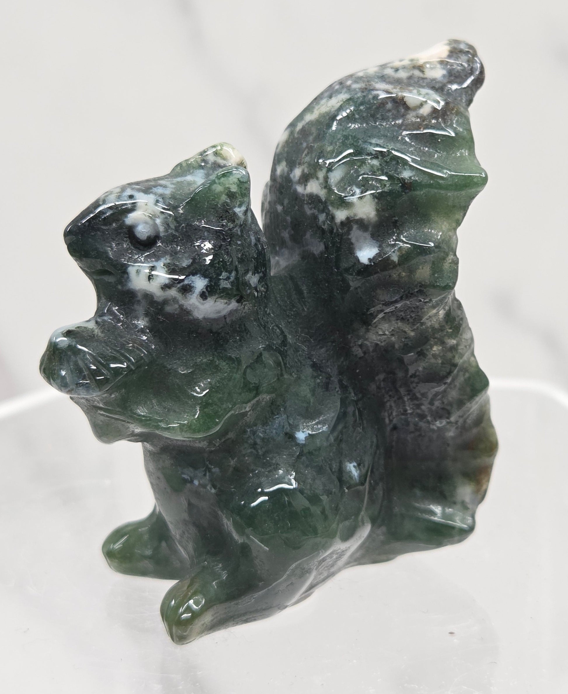 Moss Agate crystal squirrel carvings on a clear stand with a white background