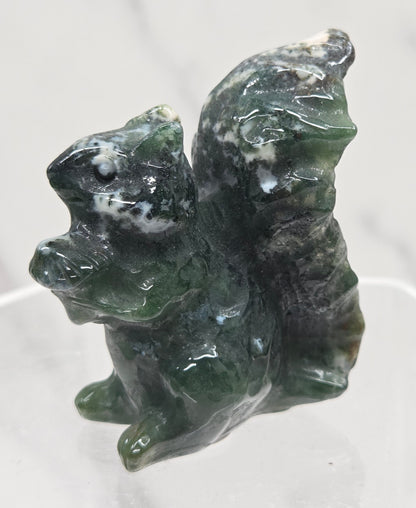 Moss Agate crystal squirrel carvings on a clear stand with a white background