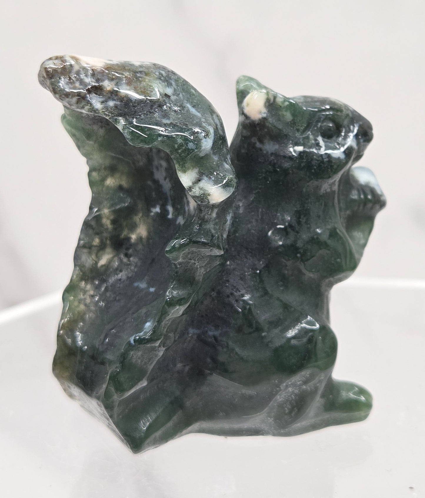 Moss Agate crystal squirrel carvings on a clear stand with a white background
