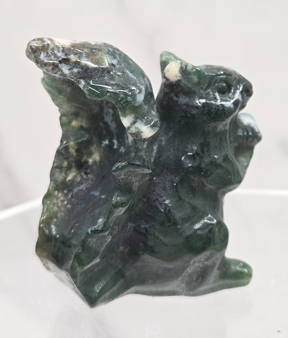 Moss Agate crystal squirrel carvings on a clear stand with a white background