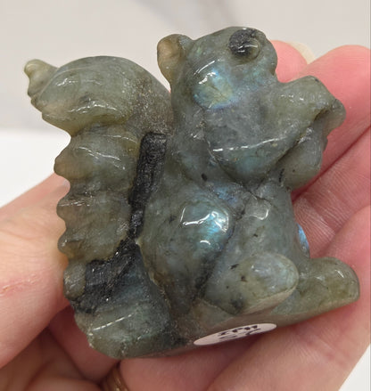 Hand holding a labradorite stone shaped like a squirrel on a white background