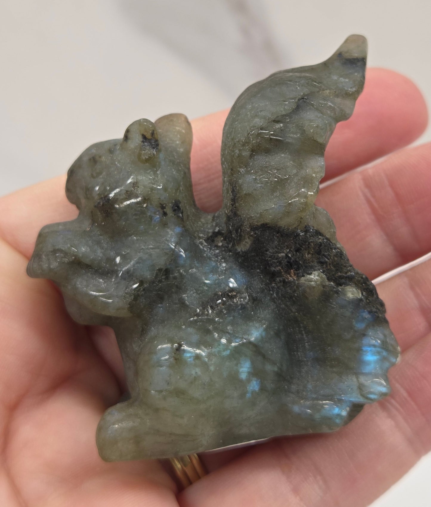 Hand holding a labradorite stone shaped like a squirrel on a white background