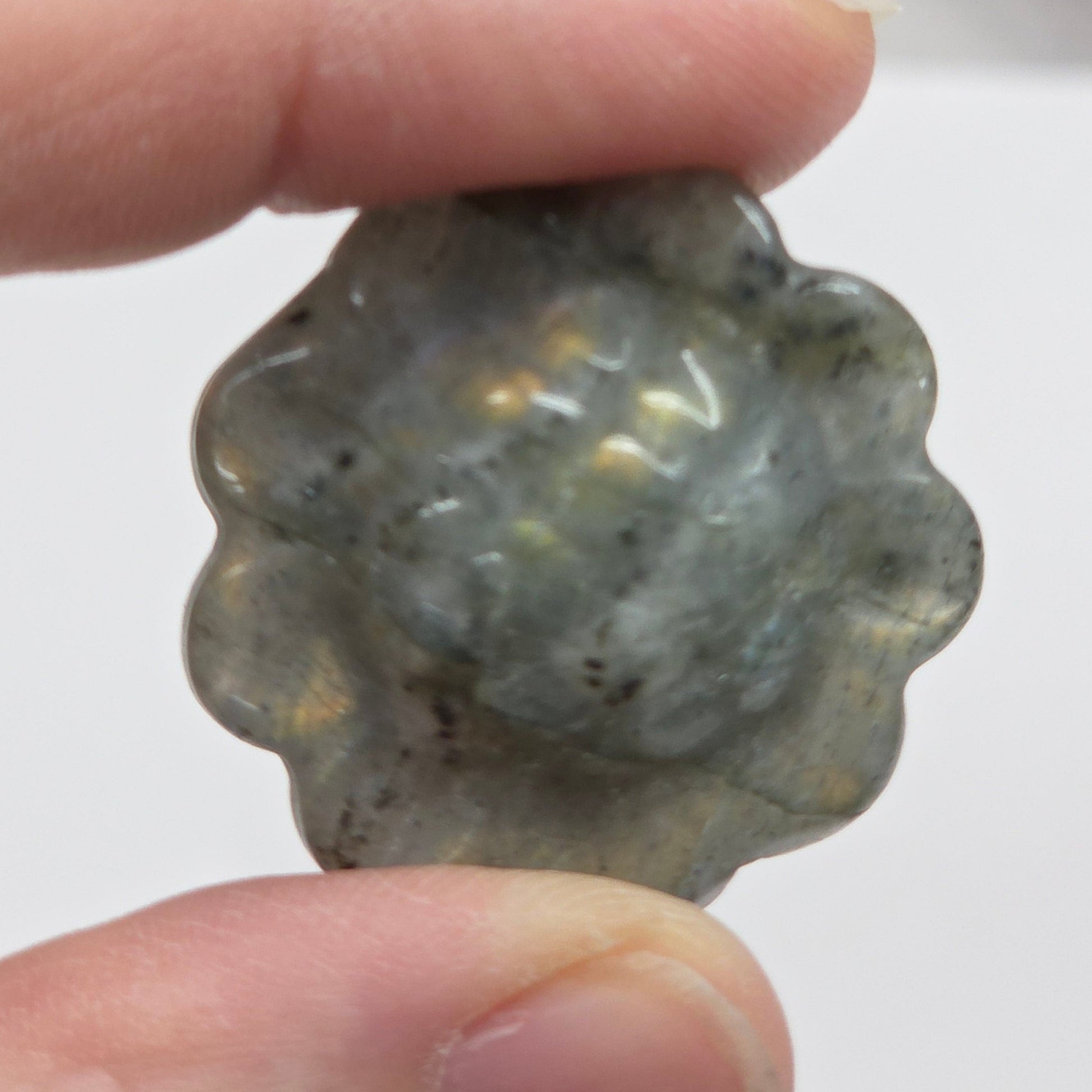 Hand holding a labradorite sunflower carving against a white background